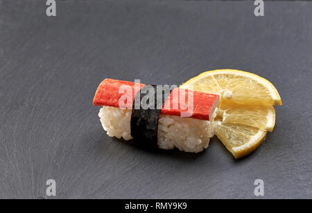 Kani japonais nigiri avec la chair de crabe artificiel sur le riz blanc, avec de la bande de nori. Sushi servi avec du citron sur la plaque d'ardoise noire. Banque D'Images