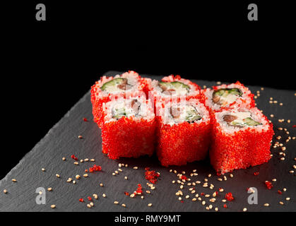 Rouleaux Philly recouvert d'oeufs de tobiko rouge, servi sur la plaque en pierre noire, décoré avec du sésame. Uramaki de Philadelphie avec le concombre, le saumon et le fromage à la crème. Banque D'Images