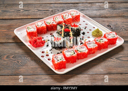 Délicieux sushi uramaki présenté sur assiette blanche, décorée de mayo, gingembre mariné et wasabi. Rouleaux de Philadelphie rempli de poisson, concombre, fromage à la crème, recouvert de tobiko rouge corail. Banque D'Images