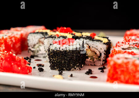 Close up of Philadelphia roule avec du thon, concombre et fromage à la crème, recouvert de caviar noir. Sushi Uramaki situé sur la plaque blanche. Banque D'Images