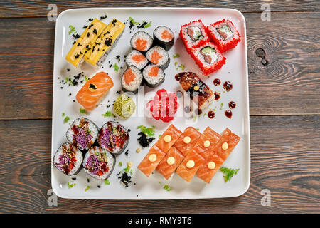 Vue de dessus de différentes sortes de nigiri, maki et uramaki. Philadelphia, fromage et rouleaux de légumes servi avec wasabi et gingembre mariné sur plaque blanche, fond de bois. Banque D'Images