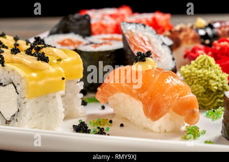 Nigiri Sake et rouleaux de fromage de près. De savoureux plats japonais. Ensemble de maki sushi uramaki et décorées avec Mayo, black caviar, servi avec wasabi sur plaque blanche. Banque D'Images