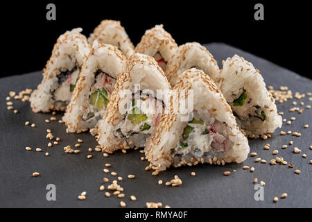 Sushi california Triangle rempli de fromage à la crème, concombre ou kappa et artificielle la chair de crabe. Uramaki couvert de sésame, présenté sur la plaque d'ardoise noire. Banque D'Images