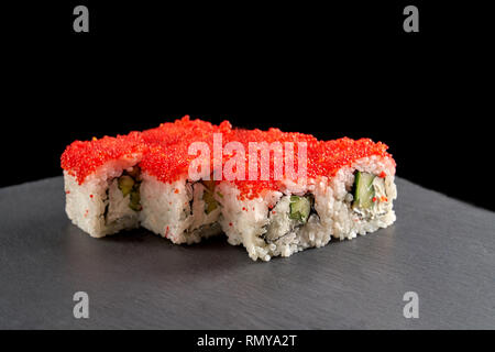 Uramaki sushi japonais traditionnel servi sur la plaque d'ardoise noire. California roll rempli de concombre, fromage à la crème et la chair de crabe, couverts de tobiko rouge corail. Banque D'Images