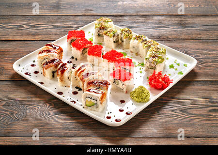 Beau dragon set de sushis, décorées avec sauce unagi, wasabi et gingembre mariné sur plaque blanche. La Californie et philadelphia rolls remplie de fromage à la crème, le concombre, l'anguille fumée et la chair de crabe. Banque D'Images