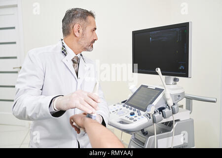 De maturité et de professionnalisme doctor holding part du patient, de faire l'examen d'ultrasons. Thérapeute utilisant sonde échographique pour le diagnostic. Médecin à la recherche à l'écran avec les résultats. Banque D'Images