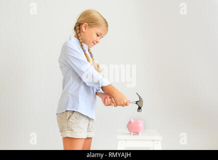 Petite fille avec un marteau par la tirelire cochon rose sur fond blanc Banque D'Images