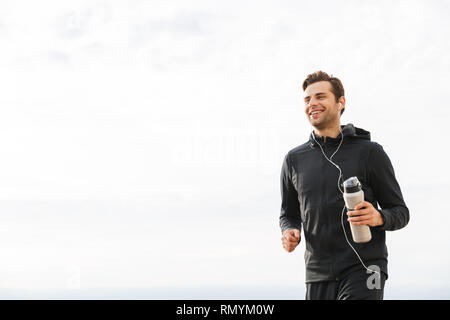 Image de sportif adultes 30s en noir sportswear et écouteurs de l'exercice et l'exécution de seaside Banque D'Images