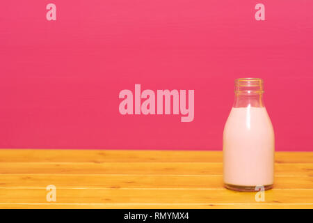 Lait frappé aux fraises dans un tiers de pinte de lait, bouteille en verre sur une table en bois contre un arrière-plan peint rose Banque D'Images