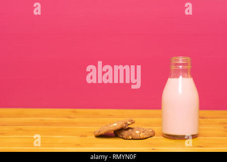 Lait frappé aux fraises dans un tiers de pinte de lait en verre bouteille et d'un biscuit aux brisures de chocolat, sur une table de bois contre un arrière-plan peint rose Banque D'Images
