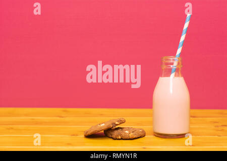 Lait frappé aux fraises avec une paille papier rétro dans une troisième pinte de lait en verre bouteille et d'un biscuit aux brisures de chocolat, sur une table de bois contre un retour rose Banque D'Images