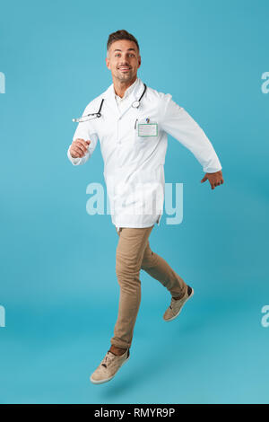 Longueur totale de droit de l'homme portant un manteau blanc medical stéthoscope et marcher tout en isolé sur fond bleu Banque D'Images