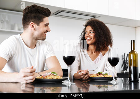 Beau jeune couple multiethnique ayant un dîner romantique à la maison, boire du vin rouge et manger des pâtes Banque D'Images