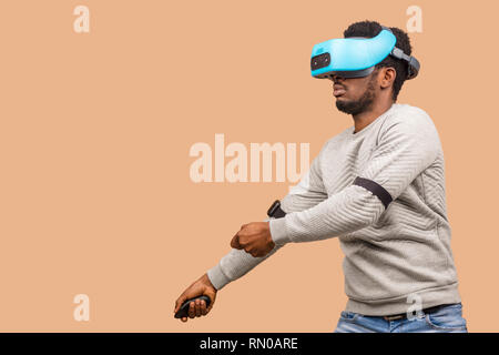 Gamer mâle teint foncé portant des lunettes de réalité virtuelle, les jeux en 3d du jeu, isolé contre mur beige studio. Banque D'Images