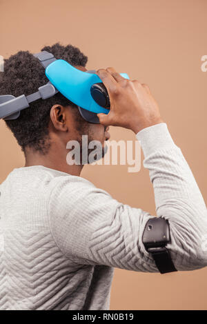 African American male gamer en blanc gilet et casque de réalité virtuelle rencontre les nouvelles technologies de l'avenir, jouer ou faire des réglages en vidéo Banque D'Images