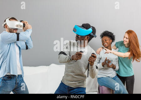 Les étudiants internationaux au repos avec divers lunettes de réalité virtuelle d'une maison, deux jeunes hommes d'hôtesse filles interracial Banque D'Images