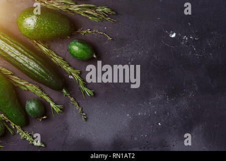 Les légumes verts, fruits et herbes assortiment sur fond noir. Copie espace vue d'en haut. Le romarin, le cumin, le concombre, l'avocat, feijoa sur la cuisine tabl Banque D'Images