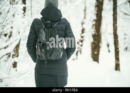 Un retour d'une belle shot youngwoman vêtu d'un manteau d'hiver noir avec sac à dos en cuir promenades dans la forêt enneigée .bois fond paysage Banque D'Images