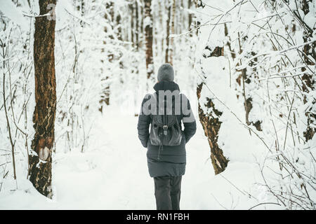 Un retour d'une belle shot youngwoman vêtu d'un manteau d'hiver noir avec sac à dos en cuir promenades dans la forêt enneigée .bois fond paysage Banque D'Images