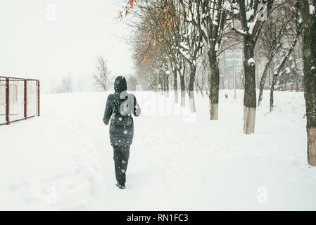 Un retour d'une belle shot youngwoman vêtu d'un manteau d'hiver noir avec sac à dos en cuir promenades dans la ville enneigée Banque D'Images