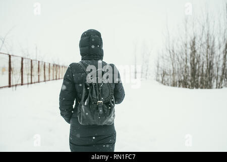 Un retour d'une belle shot youngwoman vêtu d'un manteau d'hiver noir avec sac à dos en cuir promenades dans la ville enneigée Banque D'Images