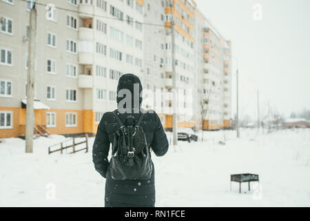 Un retour d'une belle shot youngwoman vêtu d'un manteau d'hiver noir avec sac à dos en cuir promenades dans la ville enneigée Banque D'Images