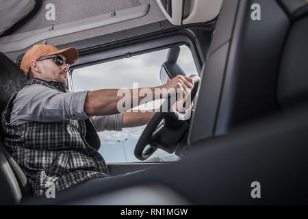 Pilote de race blanche portant des lunettes de soleil à l'intérieur de cabine de camion semi moderne. Le transport et l'industrie automobile. Conduite Commerciale. Banque D'Images