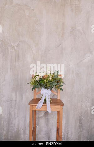 Bouquet de mariée. Mariage. mariage bouquet de fleurs blanc et vert se tient sur une chaise contre un mur gris Banque D'Images