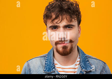 Close up of a smiling young homme barbu habillé en passant isolés sur orange Banque D'Images
