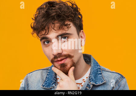 Close up of a smiling young homme barbu habillé en passant isolés sur orange Banque D'Images