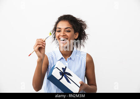 Belle jeune femme africaine debout sur fond blanc, holding gift box, montrant le pinceau Banque D'Images