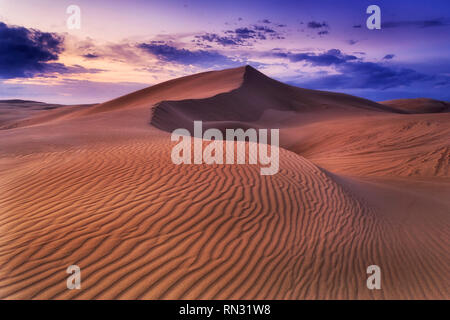 Désert de sable sans vie vide à distance au lever du soleil dans le ciel nuageux Vent sombre avec motif érodé sur dunes formant surface terrain vagues. Banque D'Images