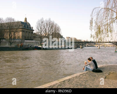 La Seine de Square du Vert Galant sur la pointe ouest de l'Île de la Cité, montrant l'Institut de France et le Pont des Arts, et deux personnes prenant une collation en plein air sur le quai : Paris, France Banque D'Images