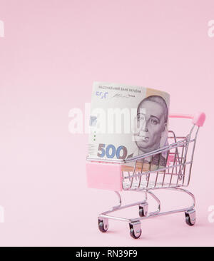 Supermarché Panier plein de billets UAH sur un fond rose avec copie Espace. Le libre-échange. marché monétaire. Style minimaliste. Chariot de supermarché en boutique. Banque D'Images