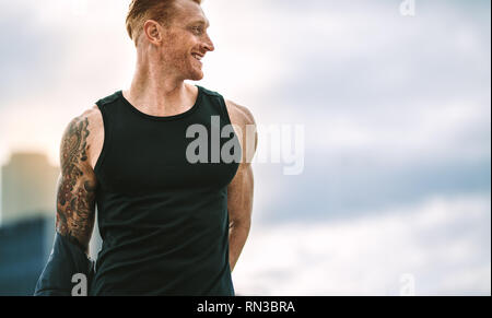 Portrait d'un homme avec le corps musclé de retirer sa chemise pour l'entraînement. Cropped shot of a smiling man standing remise en forme sur le toit étant prêt pour worko Banque D'Images