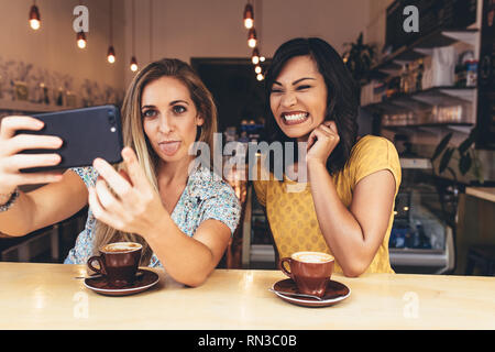 Portrait tout en tenant avec un ami selfies smiling at coffee shop. Funny female friends with mobile phone selfies at cafe. Banque D'Images