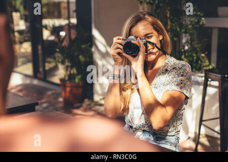 Femme à prendre des photos de ses amis avec appareil photo numérique en position assise au café. Man getting ses photos cliqué par une amie pour ce social medi Banque D'Images