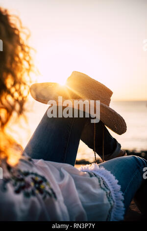 Vu de dos femme frisée se coucha et profiter de la coucher du soleil doré sur la mer - fashion style avec chapeau de cowboy sur les jambes - l'indépendance et l'inspiratio Banque D'Images