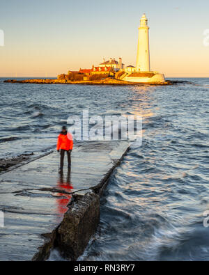 Un homme se tient sur l'île de St Mary's Causeway tandis que le soleil couchant illumine St Mary's phare sur la côte de Whitley Bay à Tyneside. Banque D'Images