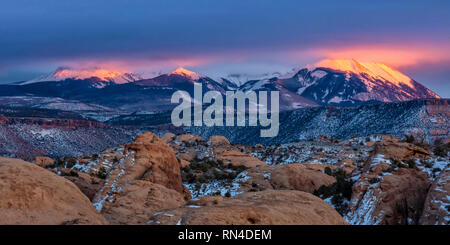 Les nuages éclairés par la lumière sur la neige sur les pics LaSal au coucher du soleil, vu de la zone de loisirs de sable dans Moab, Utah. Banque D'Images