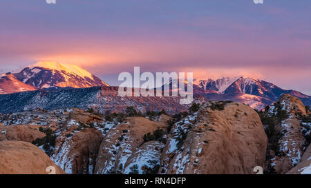 Les nuages éclairés par la lumière sur la neige sur les pics LaSal au coucher du soleil, vu de la zone de loisirs de sable dans Moab, Utah. Banque D'Images