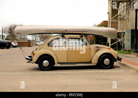 Volkswagen vieux bug avec un canot d'argent sur son toit ; VW Coccinelle avec un voile sur son toit attaché avec une corde ; prêt pour le camping ou le lac voyage. Banque D'Images