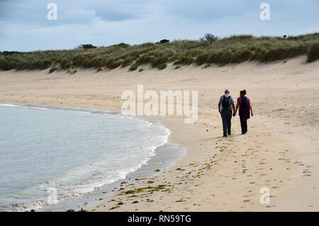 Un couple de randonneurs se tenant la main et marcher sur le sentier du littoral sur la plage de Saline Bay à Guernsey, Channel Islands.UK. Banque D'Images