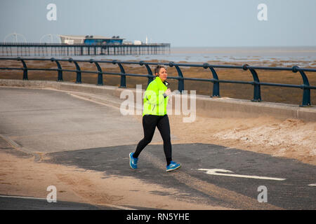 Southport, Merseyside. 17 Février, 2019. Météo britannique. Froid, lumineux ensoleillé de commencer la journée avec un ciel clair. Après un démarrage à froid 3C les températures augmenteront à un unseasonal 12C pendant la journée. La Grande-Bretagne pourrait être définie pour son jour de février le plus chaud si une poussée d'air chaud arrive la semaine prochaine, un prévisionniste des revendications. La journée la plus chaude de ce mois-ci sur fiche est 19.7C. Un jogger sur la promenade du front de mer en face de la plus ancienne jetée de fer dans le pays qui a été debout pendant plus de 150 ans et est de la ville est grand héritage de l'ère victorienne. Indicateur/AlamyLiveNews Crédit : Banque D'Images