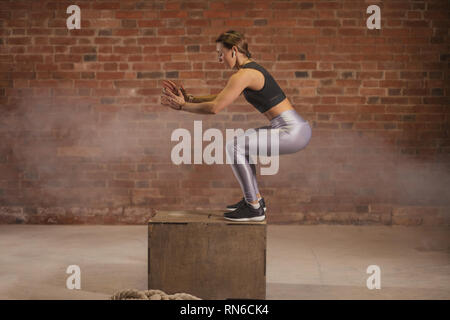 Les jeunes monter caucasian woman faisant un saut de l'exercice. La femme d'un fort s'accroupir à la salle de sport. Banque D'Images