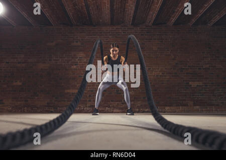 Dur travail de femme instructeur crossfit prouve que la formation des cordes sont un entraînement très dynamique qui accélère le pouls de l'athlète tout en renforçant sa Banque D'Images