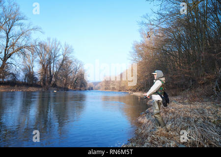 Une jeune femme attrayante attire les poissons avec une roue tournante, debout sur le bord d'une rivière sur une journée ensoleillée de printemps Banque D'Images