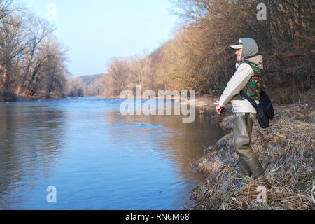 Une jeune femme attrayante attire les poissons avec une roue tournante, debout sur le bord d'une rivière sur une journée ensoleillée de printemps Banque D'Images