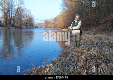 Une jeune femme attrayante attire les poissons avec une roue tournante, debout sur le bord d'une rivière sur une journée ensoleillée de printemps Banque D'Images