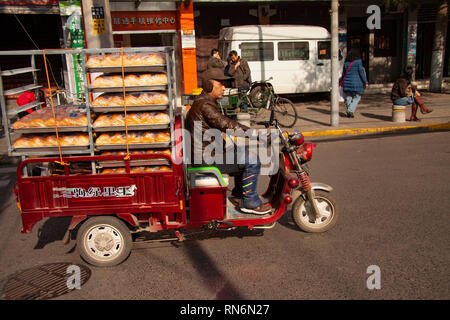 Chinese man riding un cyclomoteur fret chargé avec du pain du boulanger dans une rue de la Chine. Les vélos-cargos de marchandises ou de cyclomoteurs sont populaires transport en Chine. Être Banque D'Images